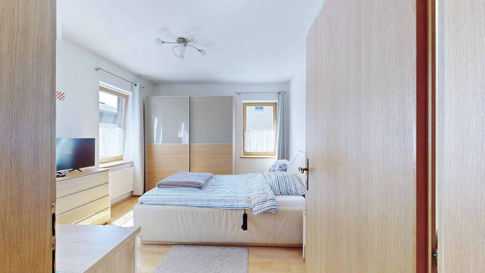 Helles Schlafzimmer mit Doppelbett, Schiebetürenschrank und zwei Fenstern für viel Tageslicht.