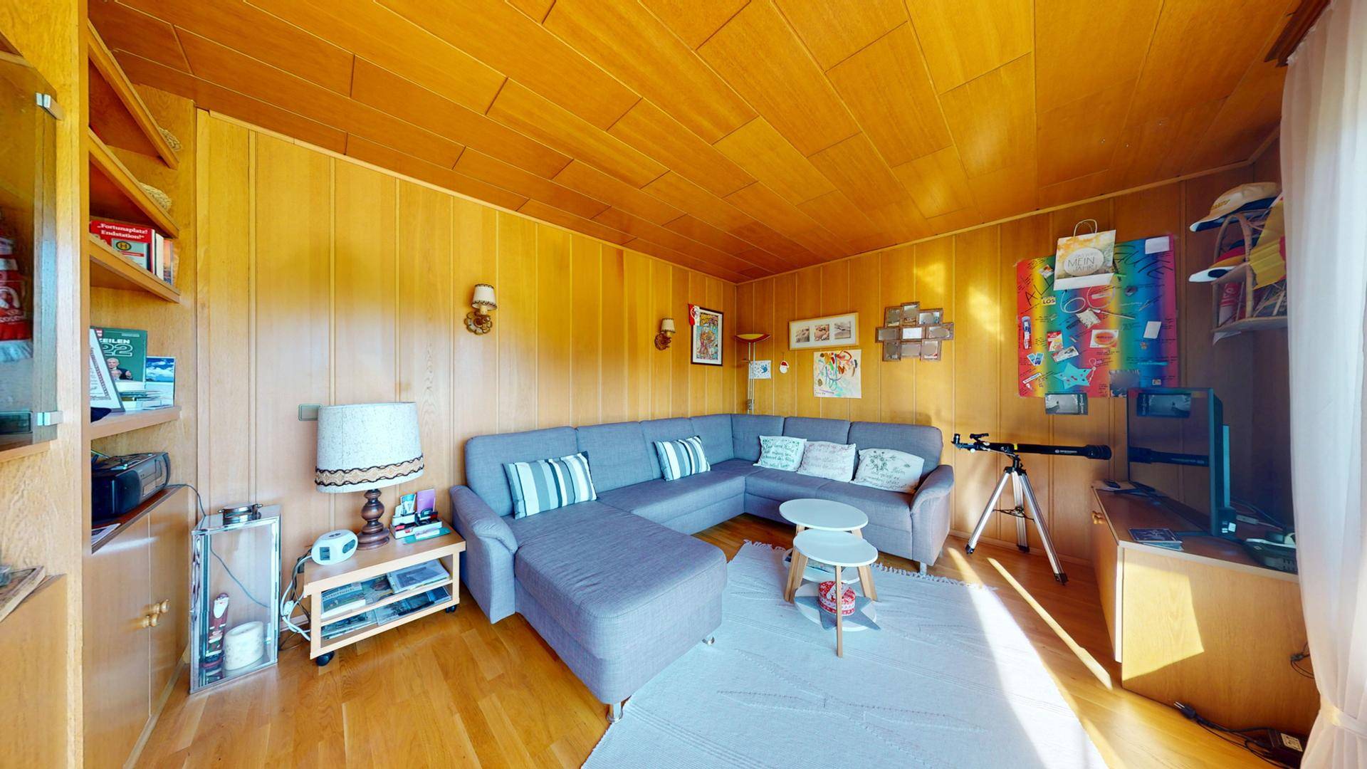 Geräumiges Wohnzimmer mit Holzvertäfelung, bequemer Sitzecke und einem Teleskop für die Aussicht.