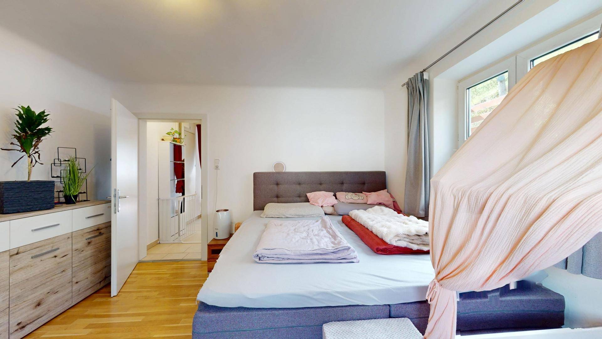 Geräumiges Schlafzimmer mit Doppelbett, Holzkommode und Zugang zu einem weiteren Raum.