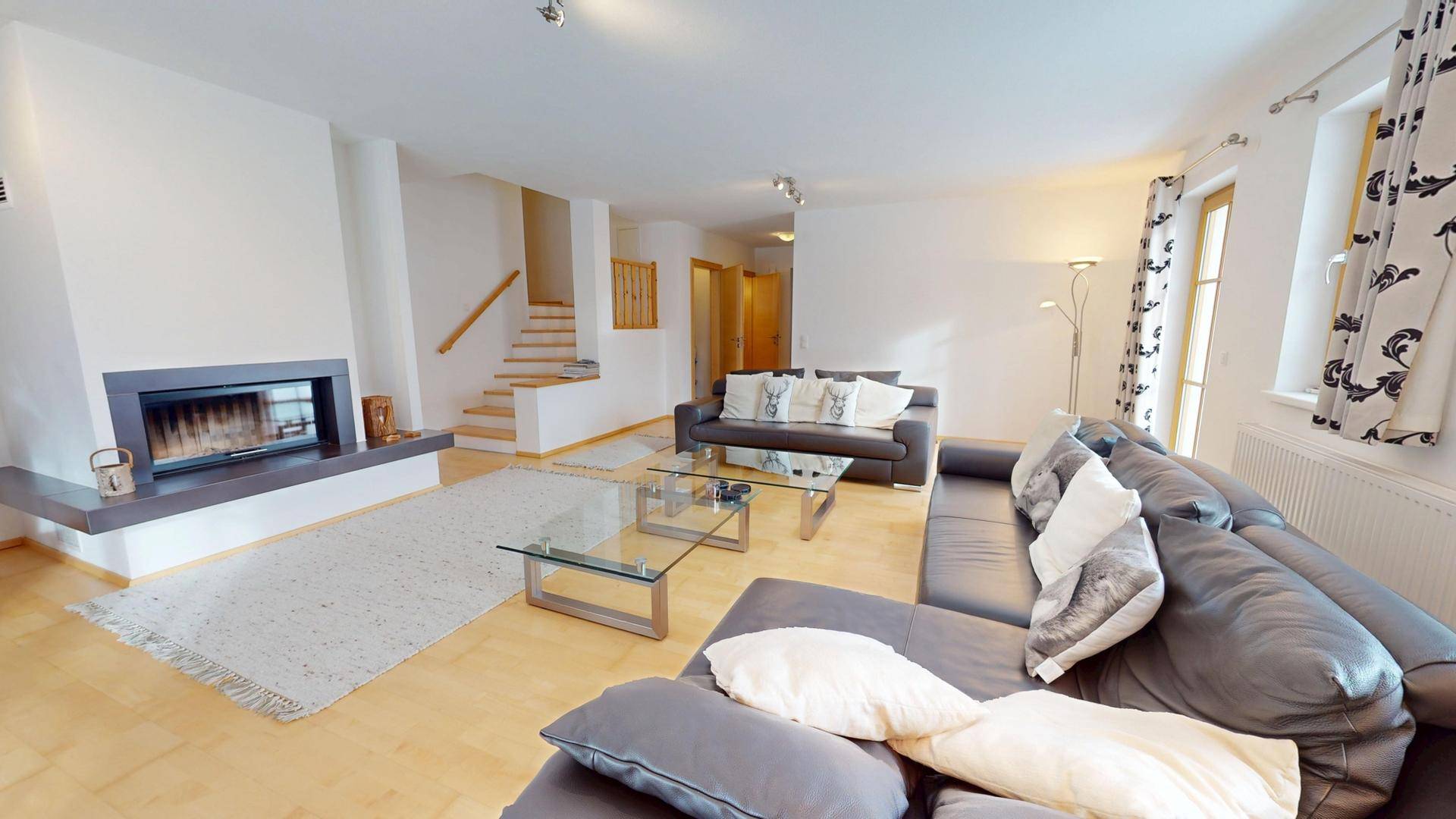 Helles Wohnzimmer mit Kamin, Ledersofas und Zugang zu einer Holztreppe.