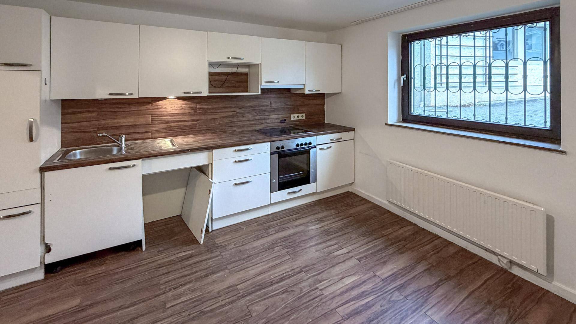 Funktionale Küche mit weißen Schränken, Holzoptik-Arbeitsplatte und Fenster.