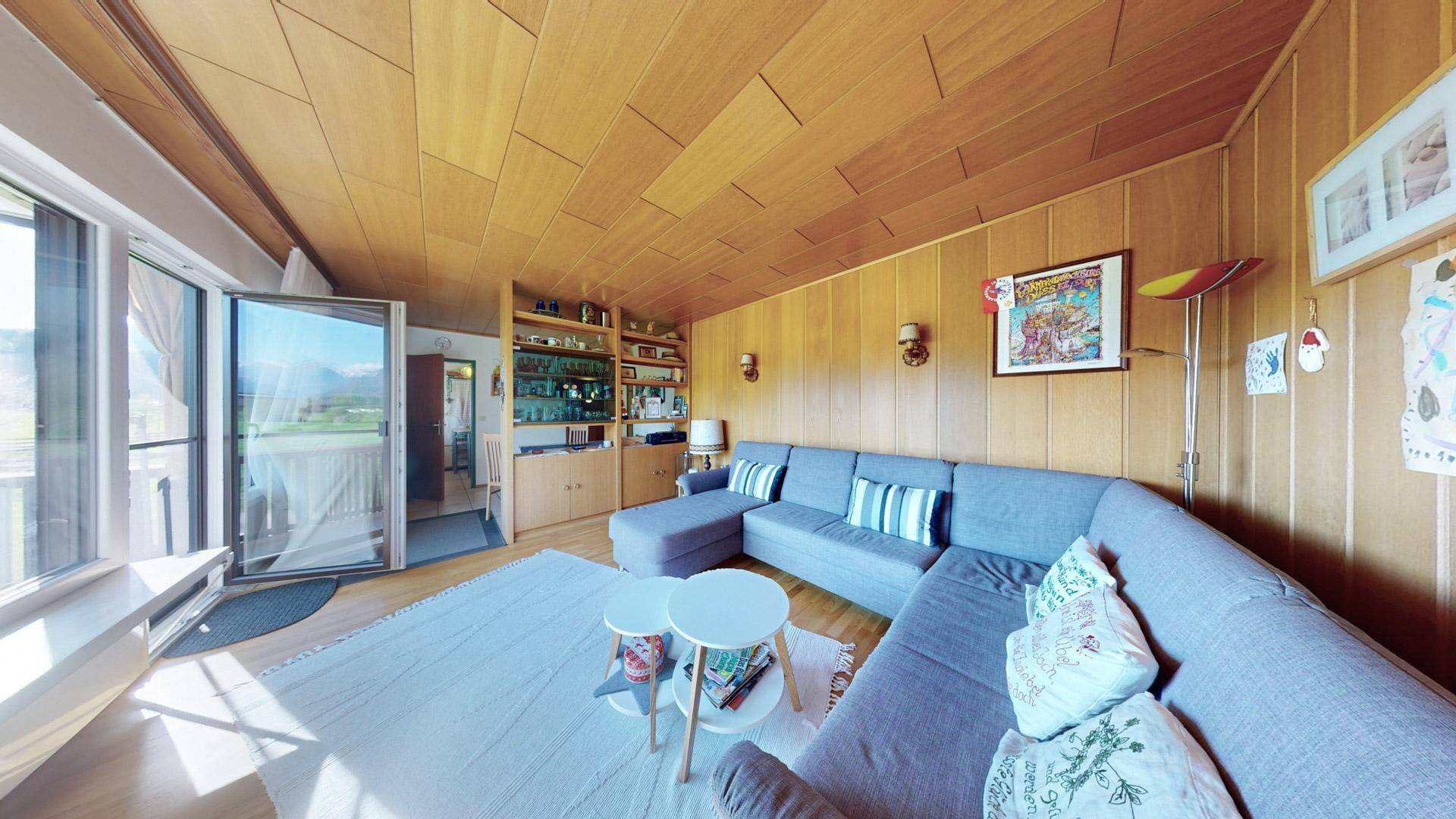 Geräumiges Wohnzimmer mit L-förmigem Sofa, Holzvertäfelung und Balkonzugang.