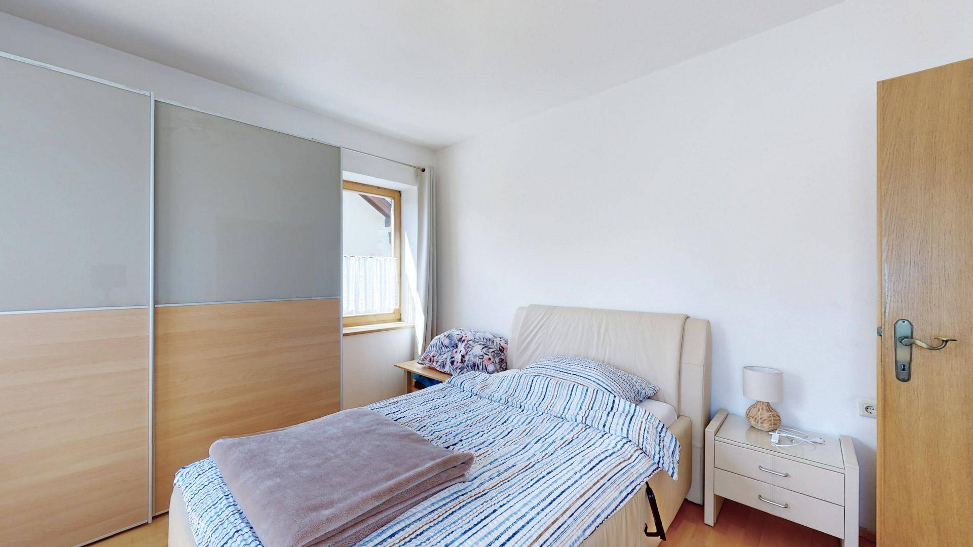 Schlafzimmer mit gemütlichem Bett, Nachttisch und Blick auf den Kleiderschrank.