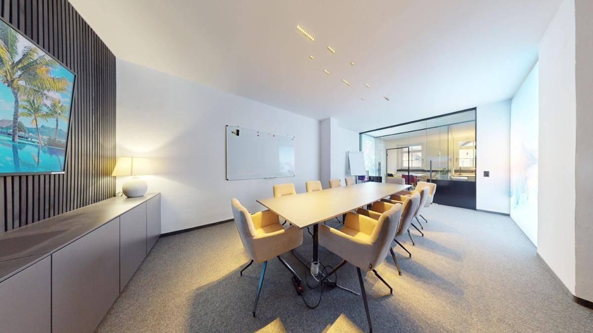 Heller Konferenzraum mit modernem Design, langem Tisch, bequemen Stühlen und einer Glaswand zum angrenzenden Bereich.