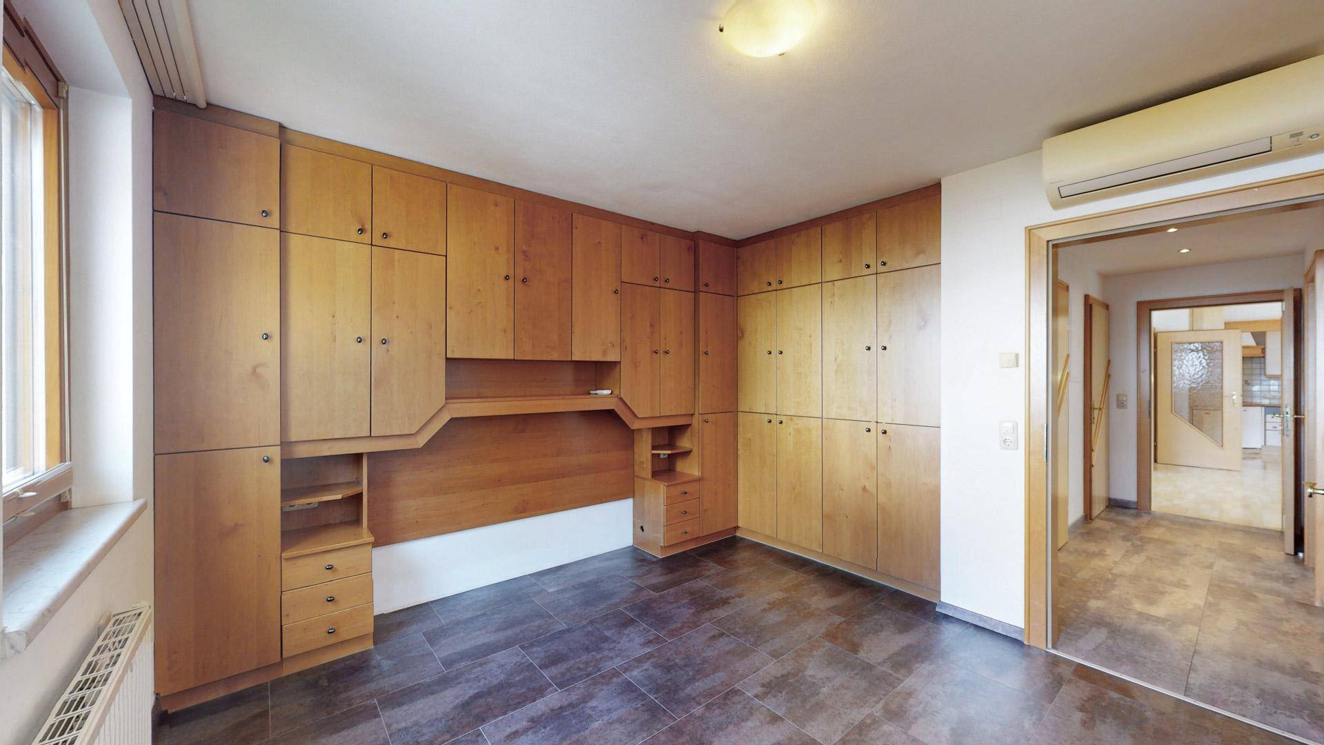 Schlafzimmer mit maßgefertigten Holzschränken und dunklem Fliesenboden, bietet viel Stauraum.