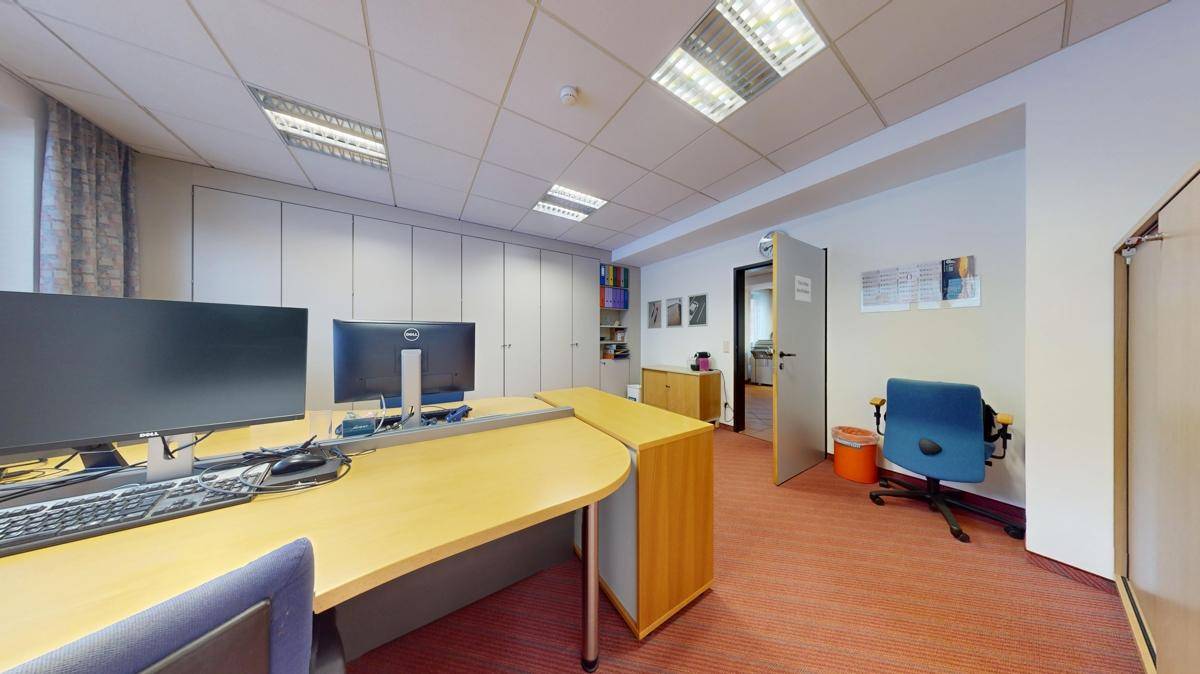Büro mit Teppichboden, Schreibtisch und integrierten Schränken, die eine aufgeräumte Arbeitsumgebung ermöglichen.
