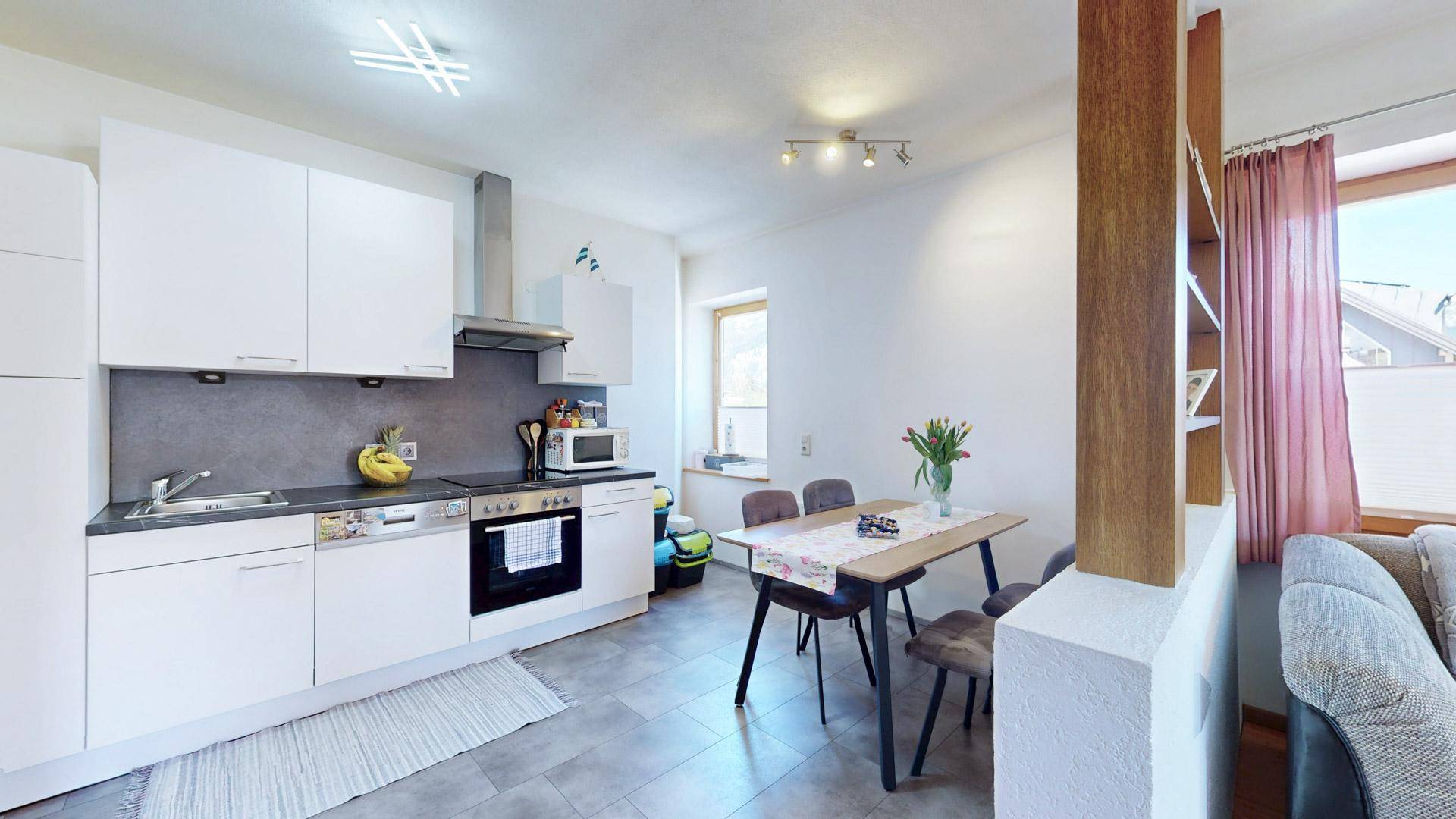 Moderne Einbauküche mit weißen Fronten, Induktionskochfeld und kleinem Essbereich am Fenster.
