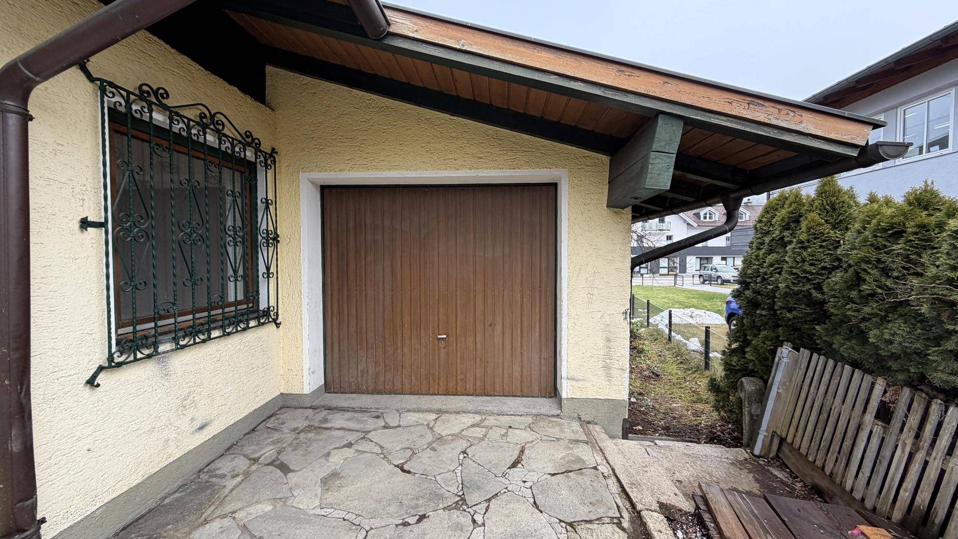 Einzelgarage mit Holztor und gepflastertem Vorplatz, umgeben von Grün.