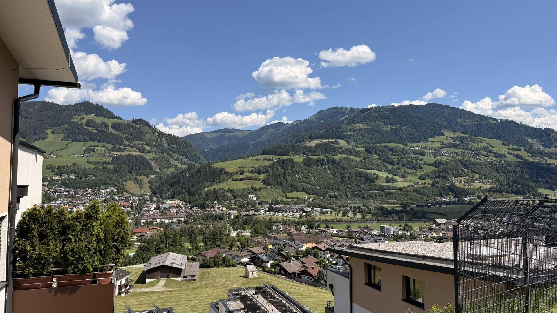 Weitläufiger Panoramablick über ein Tal mit einer Stadt und grünen, bewaldeten Bergen unter blauem Himmel.