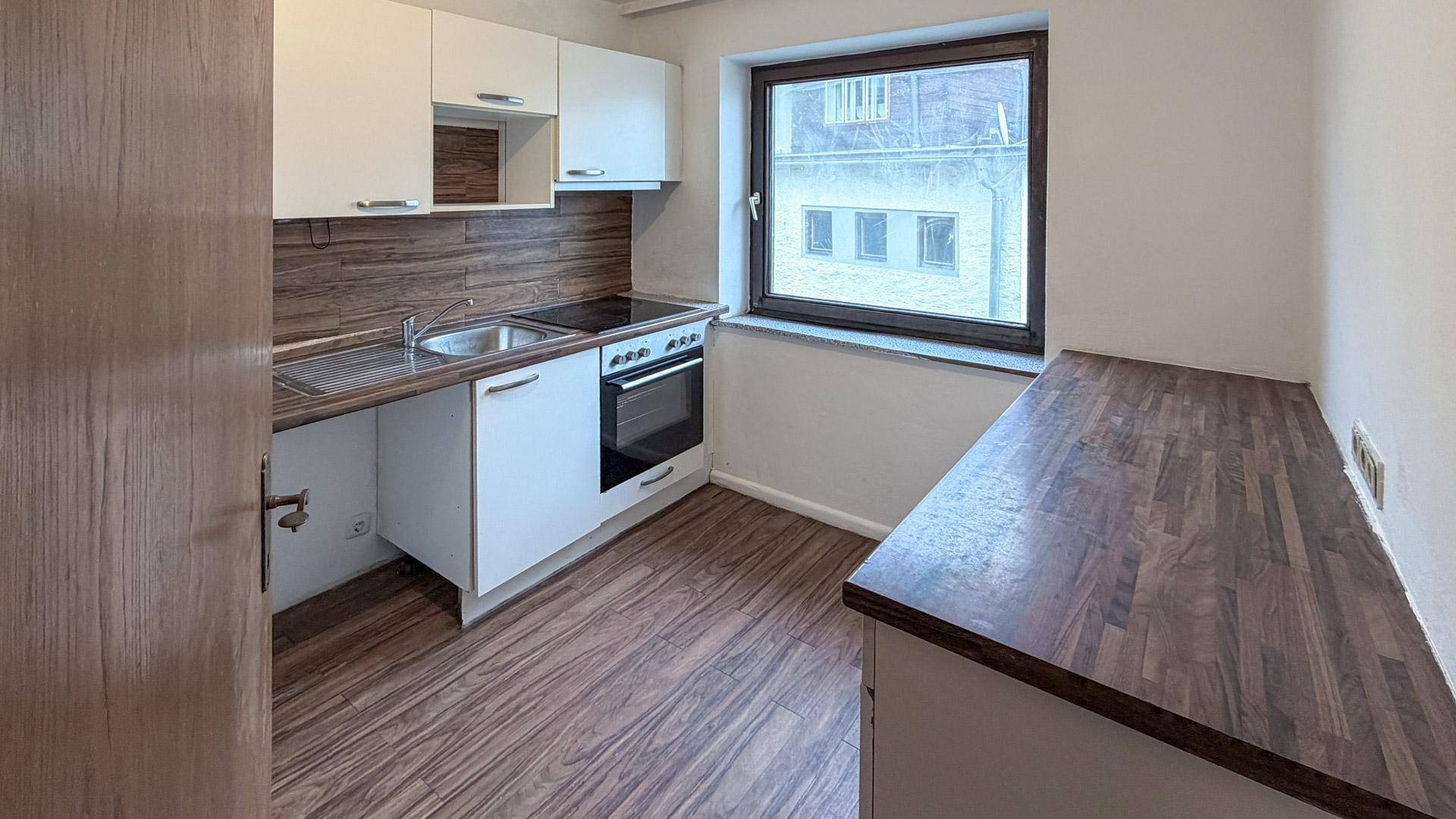 Kleine Küche mit weißen Schränken, Holzoptik-Arbeitsplatte und Fenster.