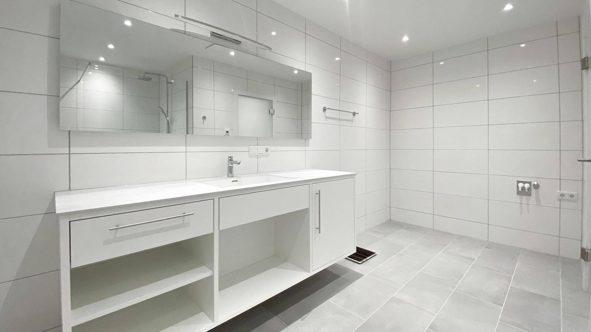 Helles, modernes Badezimmer mit großen weißen Wandfliesen, Doppelwaschtisch und großem Spiegelschrank.