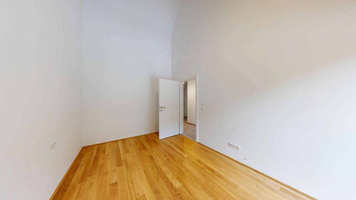 Geräumiges Zimmer mit Holzboden und einer offenen Tür, die den Blick in den Flur freigibt.