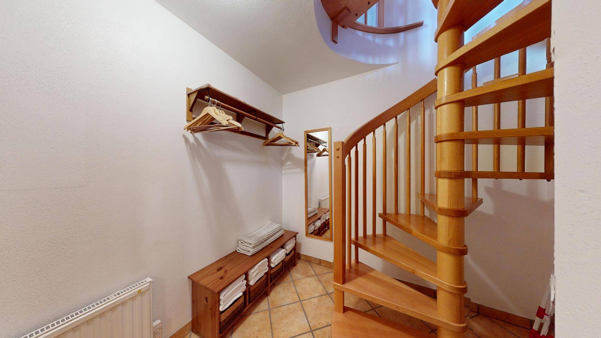 Flur mit einer eleganten Holzwendeltreppe und praktischer Ablage für Kleidung.
