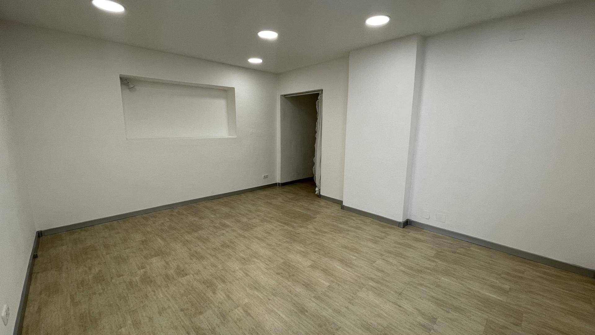Leerer Raum mit Holzoptikboden, weißen Wänden, einer Nische und Deckenstrahlern.