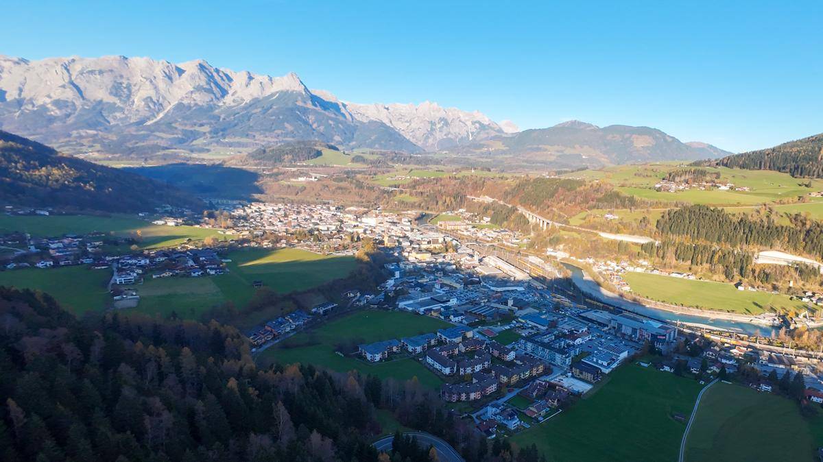 Weitläufige Luftaufnahme einer Stadt im Tal, umgeben von majestätischen Bergen und grünen Wäldern.