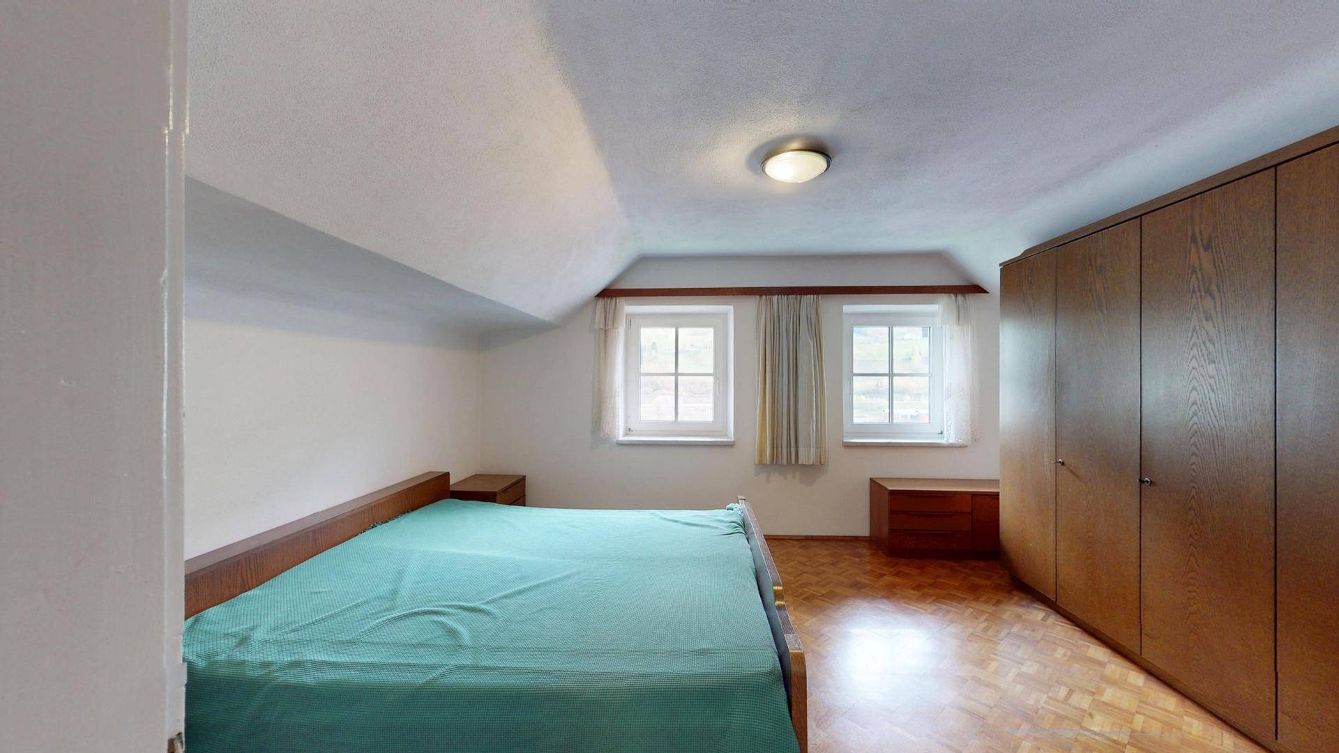 Schlafzimmer im Dachgeschoss mit Doppelbett, Einbauschrank und schrägen Wänden.