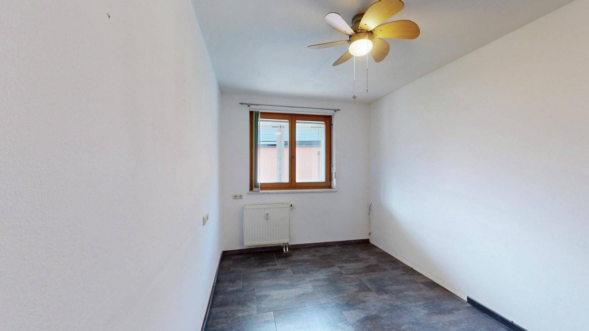 Helles Zimmer mit dunklem Fliesenboden, Deckenventilator und Fenster.