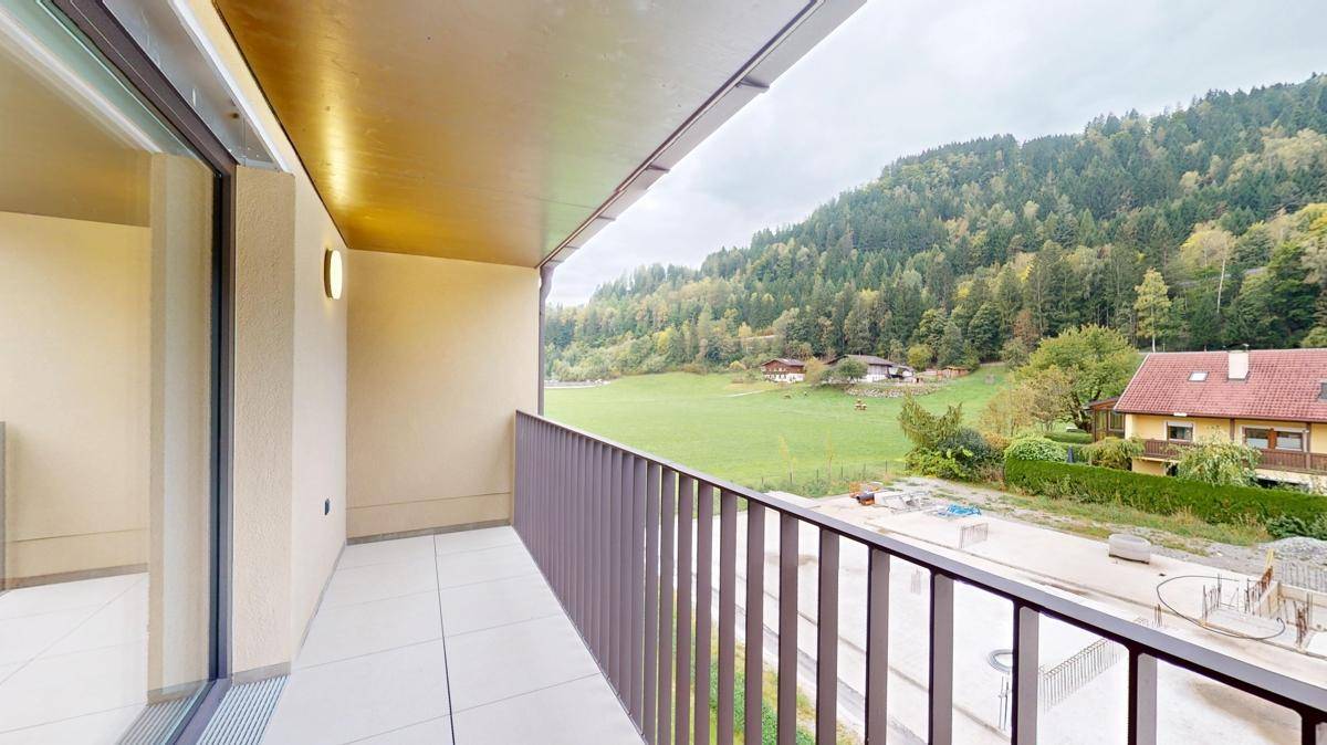 Geräumiger Balkon mit Fliesenboden und weitem Blick auf die grüne Landschaft und Berge.