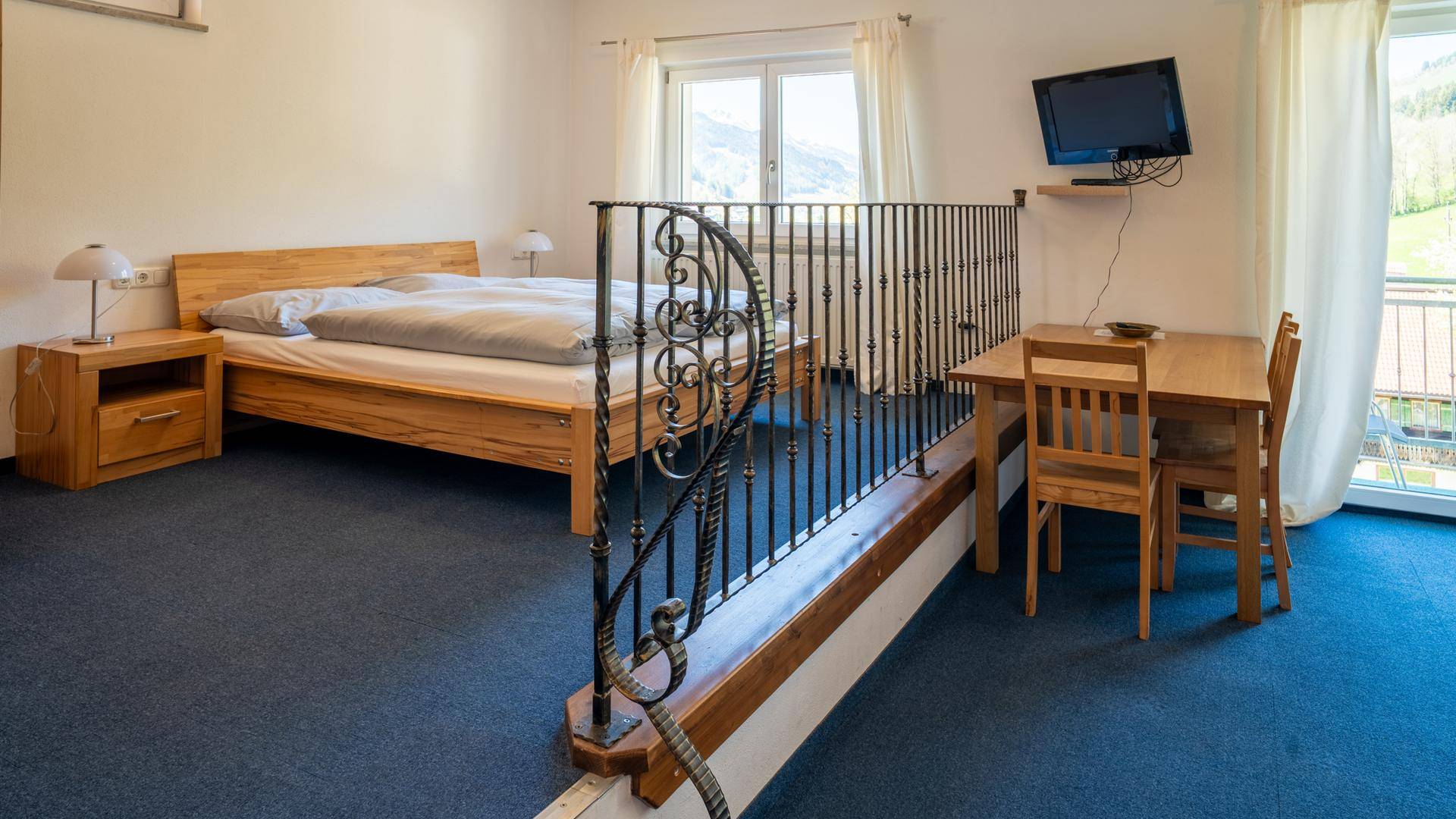 Helles Schlafzimmer mit Holzdoppelbett, Teppichboden und Blick auf die grüne Landschaft.