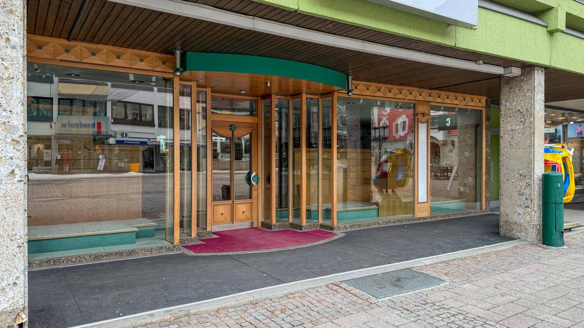 Eingangsbereich eines Geschäfts mit großen Schaufenstern, Holzelementen und Blick auf die Straße.