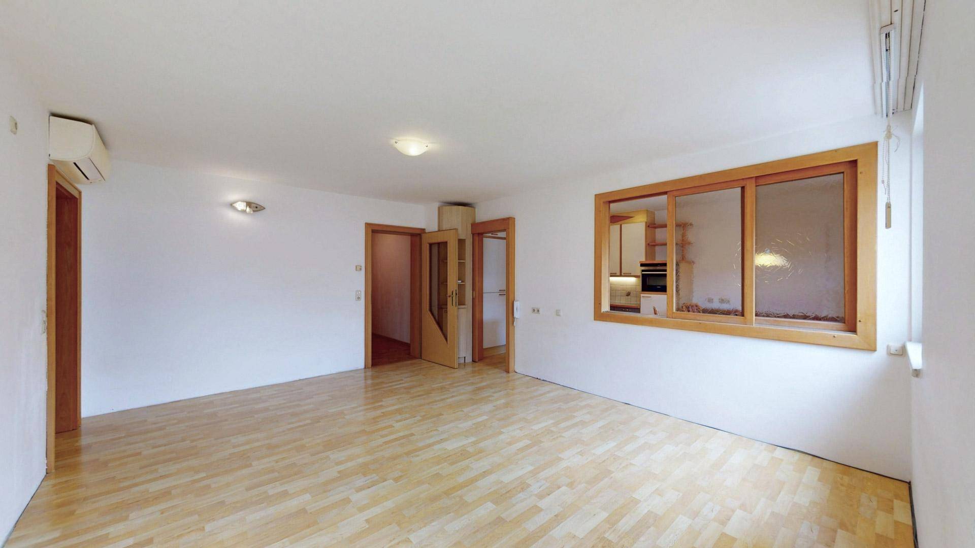 Geräumiger Wohnbereich mit Holzboden und einer Durchreiche zur Küche, ideal für offenes Wohnen.