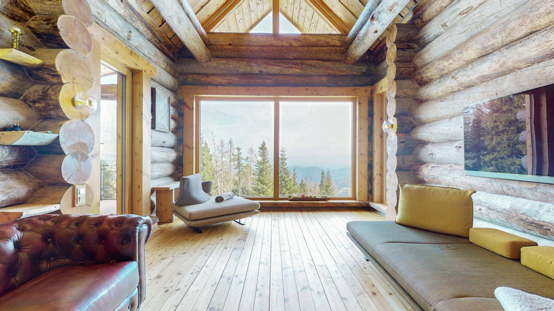 Lichtdurchflutetes Wohnzimmer mit Holzbalken und Panoramafenstern, die den Blick auf die Natur freigeben.