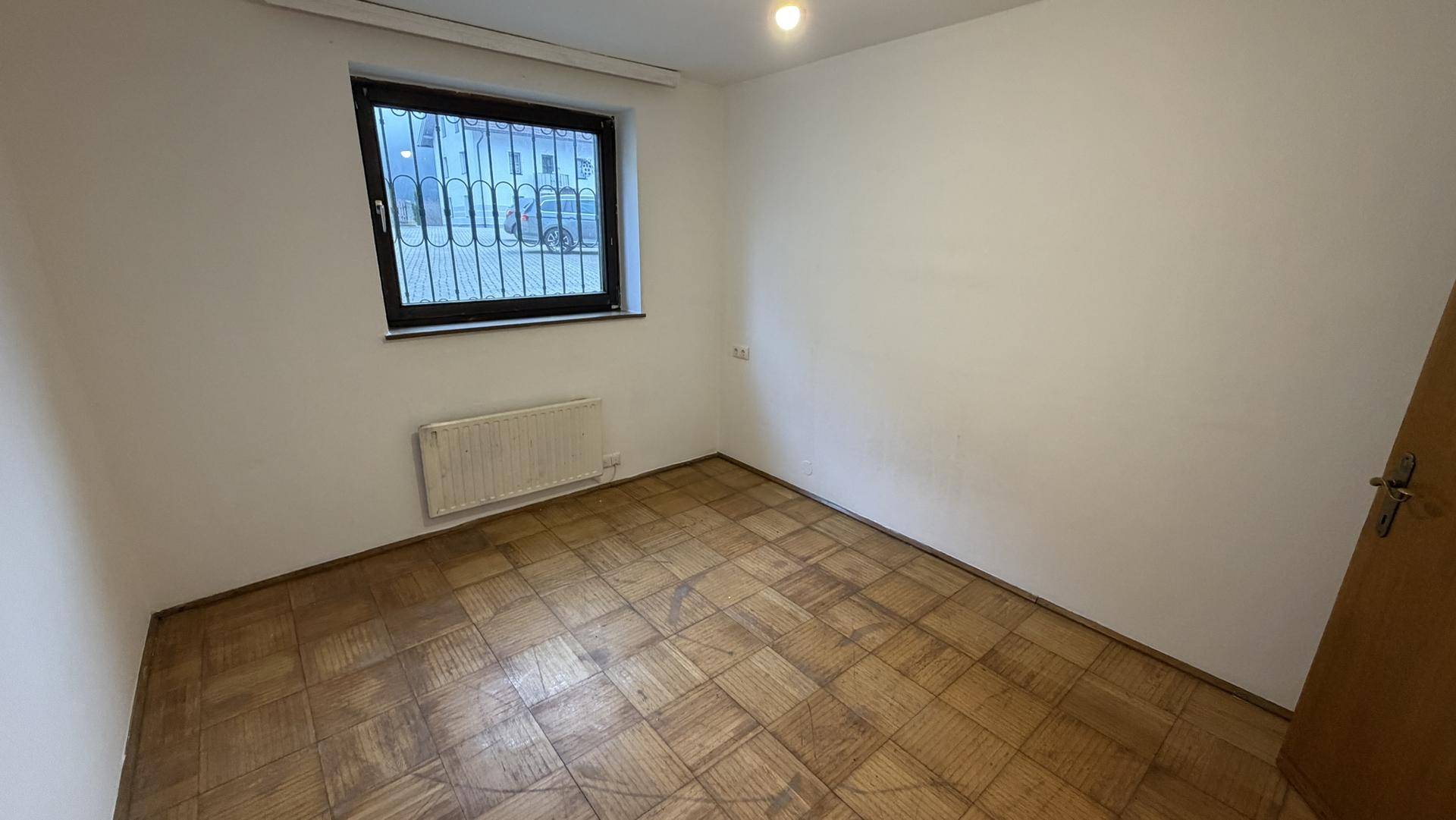 Helles Zimmer mit Parkettboden und Fenster mit Blick auf die Umgebung.
