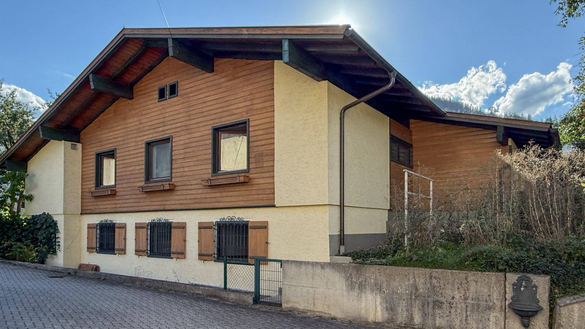Rückansicht des traditionellen Hauses mit Holzfassade, Fensterläden und weitem Blick auf die umliegende Berglandschaft.