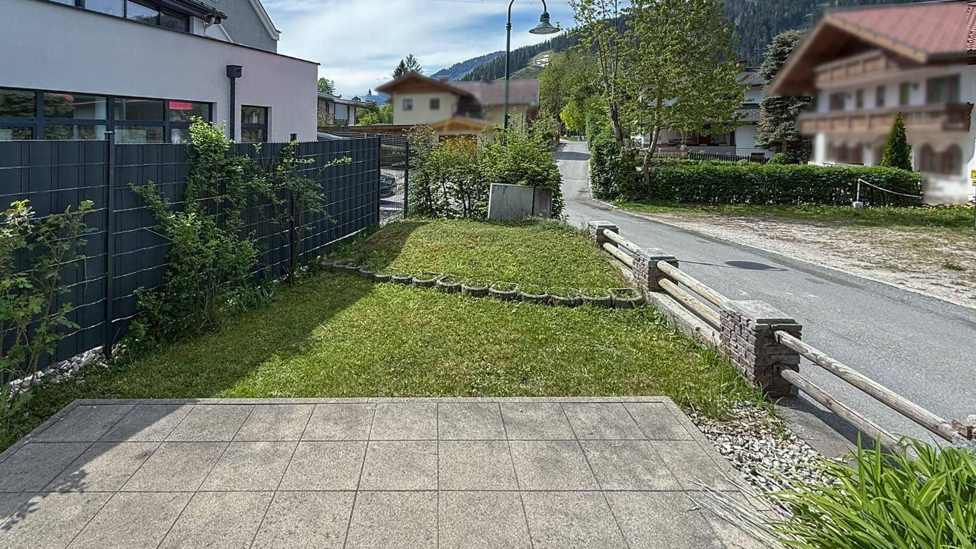 Gepflasterte Terrasse mit angrenzendem Rasen und Blick auf die ruhige Wohngegend und Berge.
