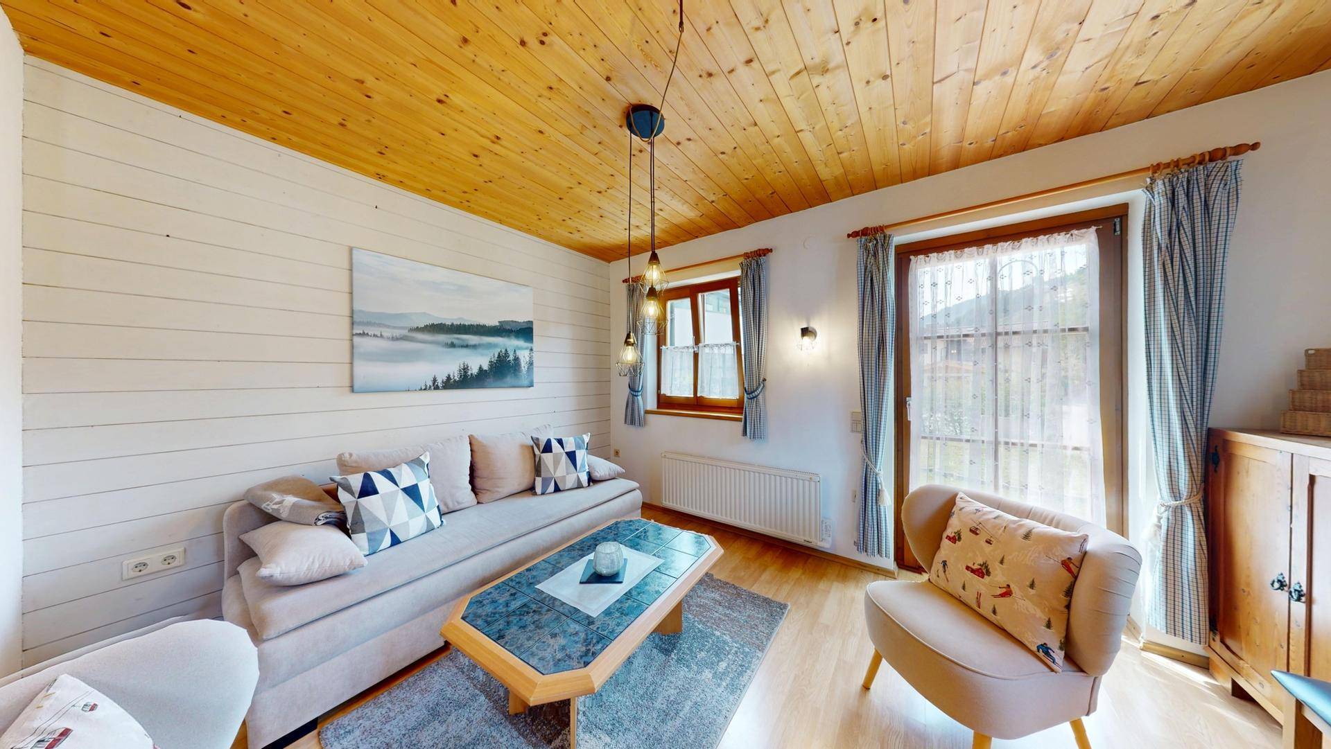 Helles Wohnzimmer mit bequemer Couch, Holzbalkendecke und Zugang zum Außenbereich.