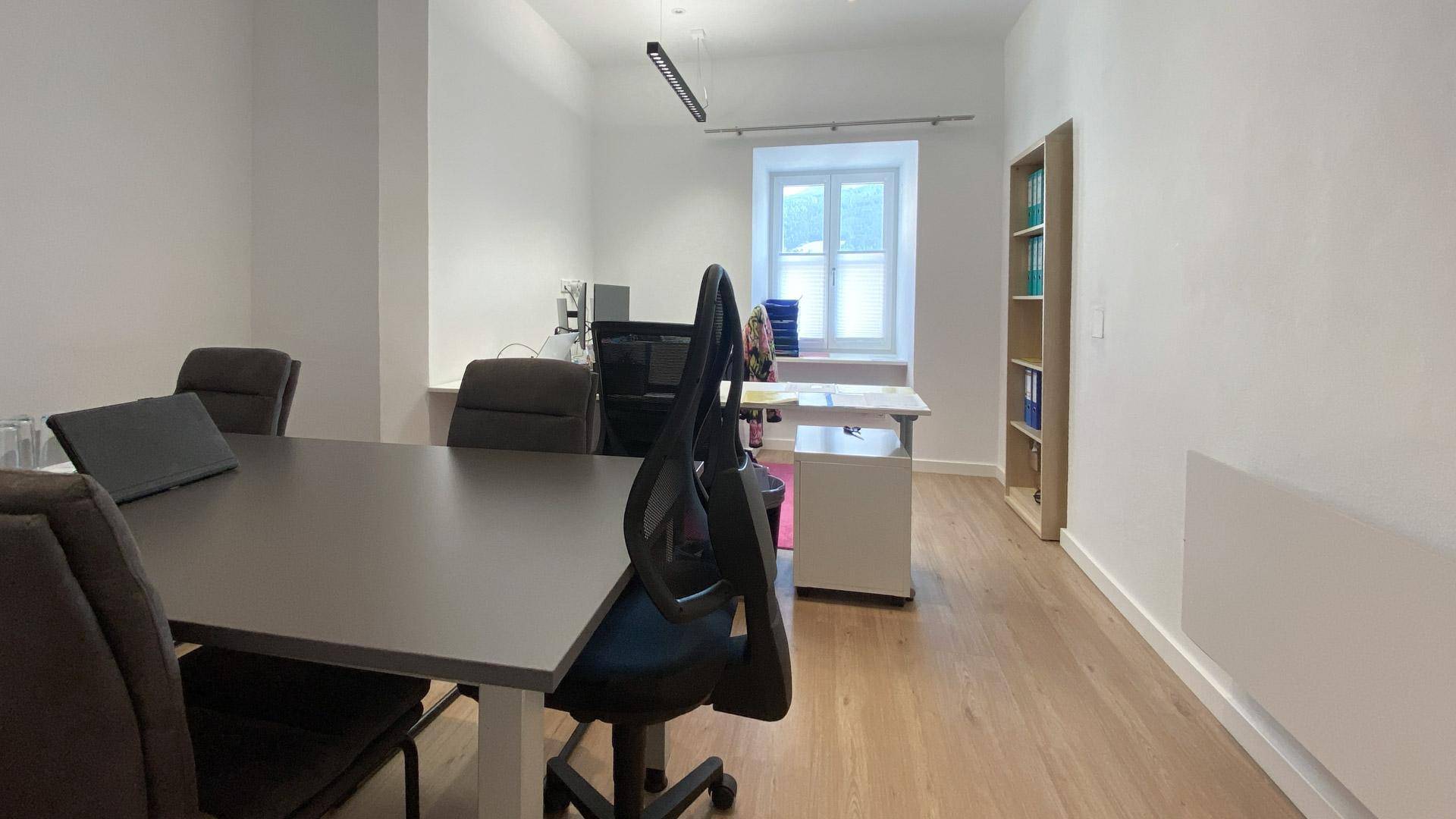 Moderner Büroraum mit großem Konferenztisch, hellem Holzfußboden und natürlichem Lichteinfall.