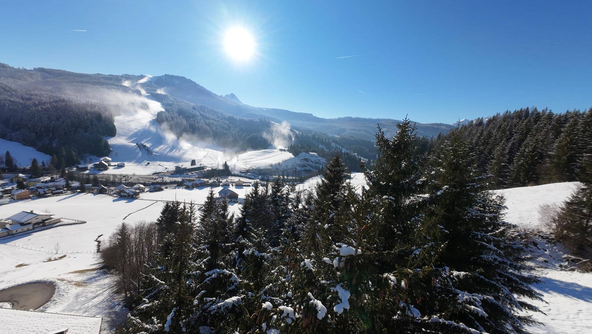 Panoramablick auf eine verschneite Berglandschaft mit Skipisten unter blauem Himmel.