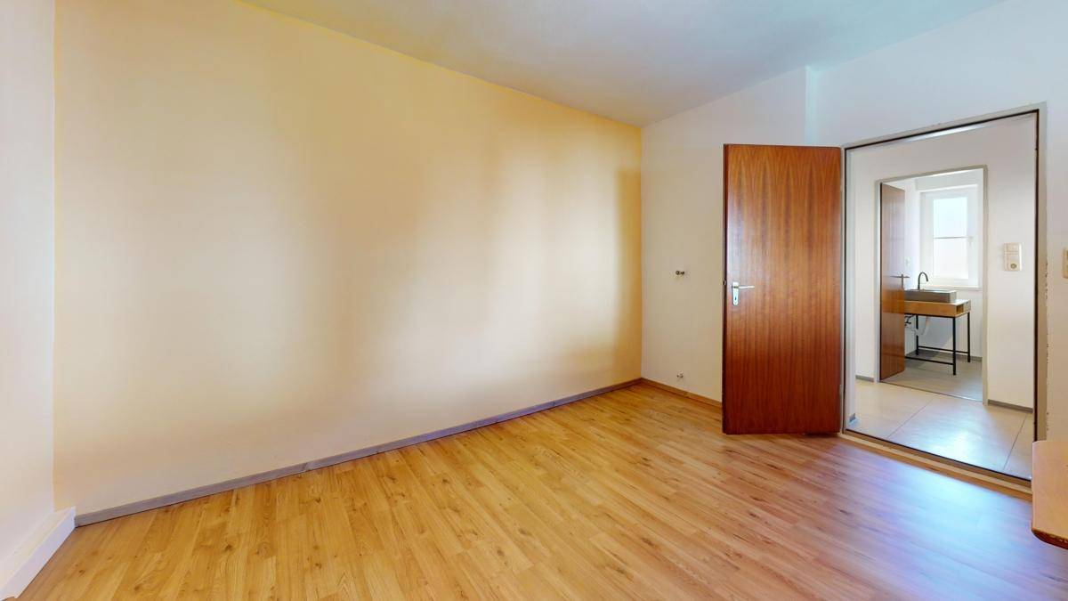 Geräumiges Zimmer mit Holzboden und Zugang zu einem angrenzenden Badezimmer, hell und funktional.