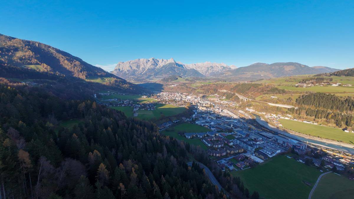 Panoramablick auf eine Stadt in einem Tal, umgeben von Bergen und weiten grünen Flächen.