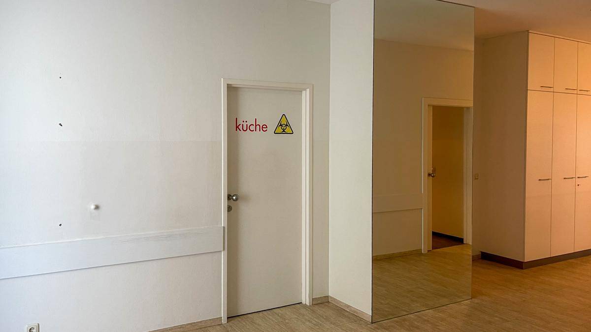 Heller Flur mit weißer Tür, die zur Küche führt, und einem großen Spiegelelement an der Wand.