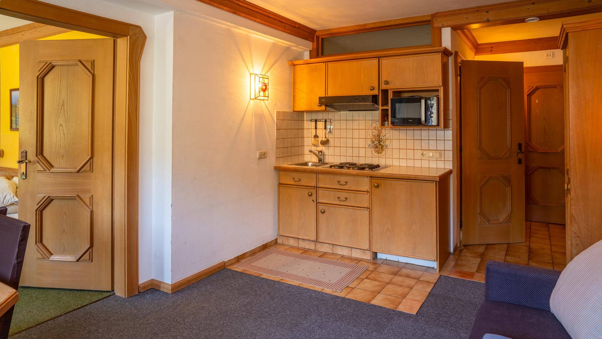Kleine Küchenzeile mit Holzschränken, Fliesenboden und integrierter Kochplatte.