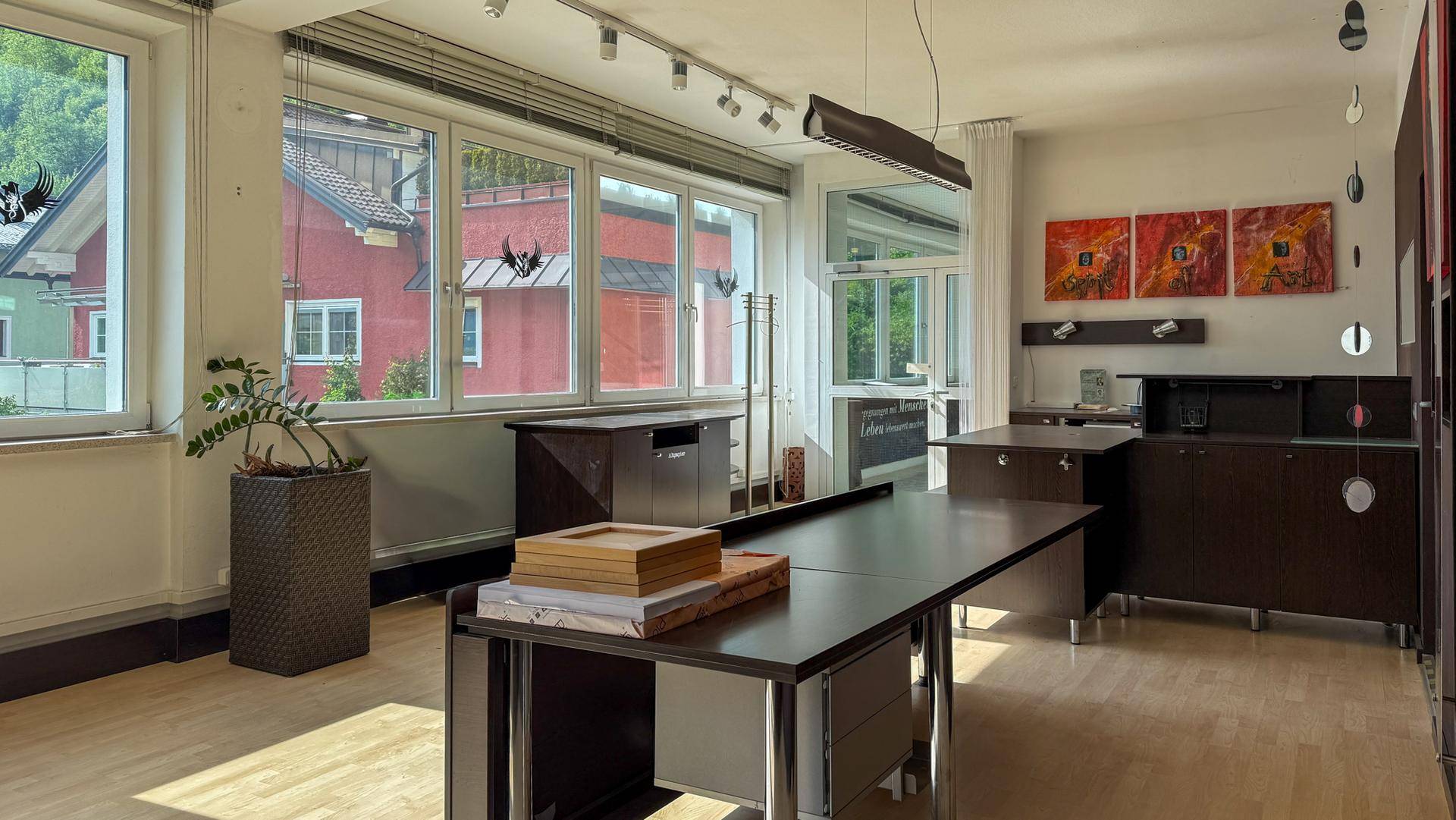 Bürofläche mit viel Tageslicht, Holzboden und dunklen Büromöbeln, die eine professionelle Atmosphäre schaffen.