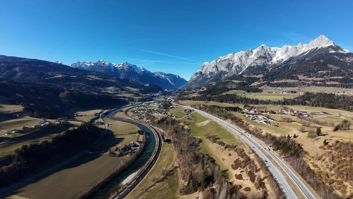 Breite Luftaufnahme eines Tals mit schneebedeckten Bergen, einem Fluss und einer Autobahn.