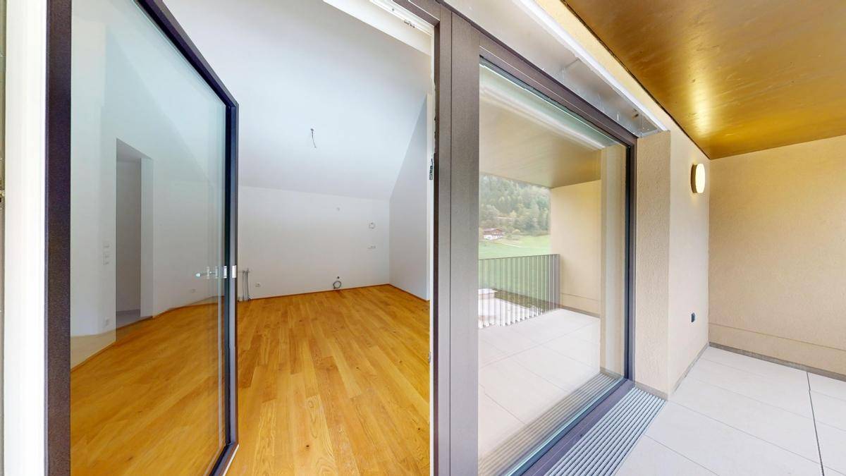 Heller Innenraum mit Holzboden, sichtbar durch die große Balkontür, die nach draußen führt.