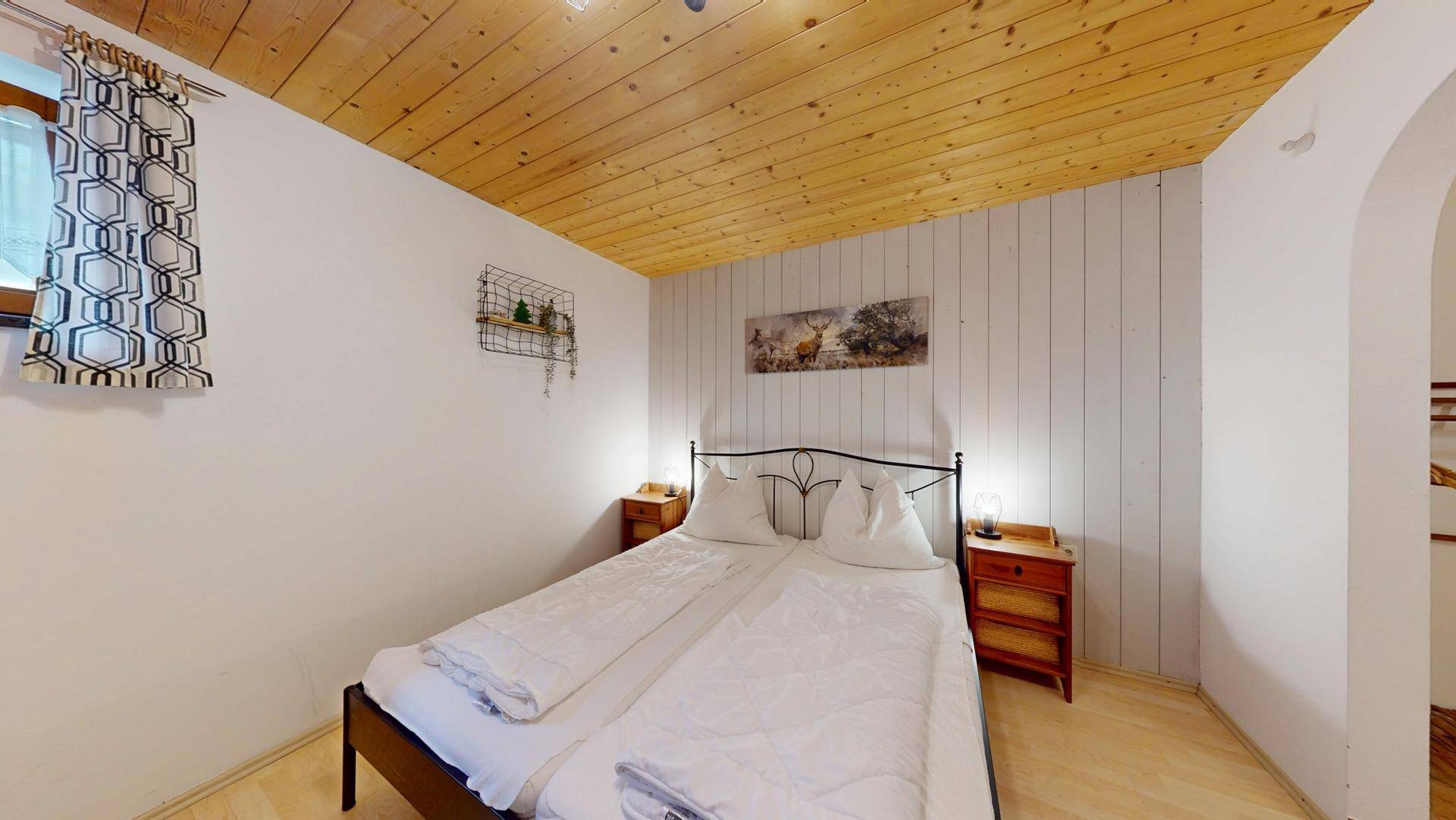 Schlafzimmer mit Doppelbett, Holzbalkendecke und schlichten Nachttischen.