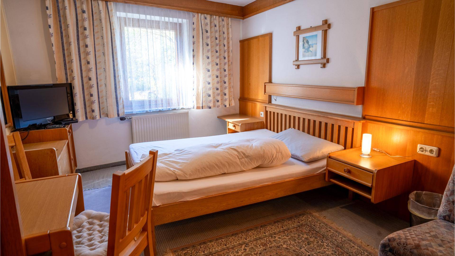 Gemütliches Schlafzimmer mit Einzelbett, Holzmöbeln und Teppichboden.