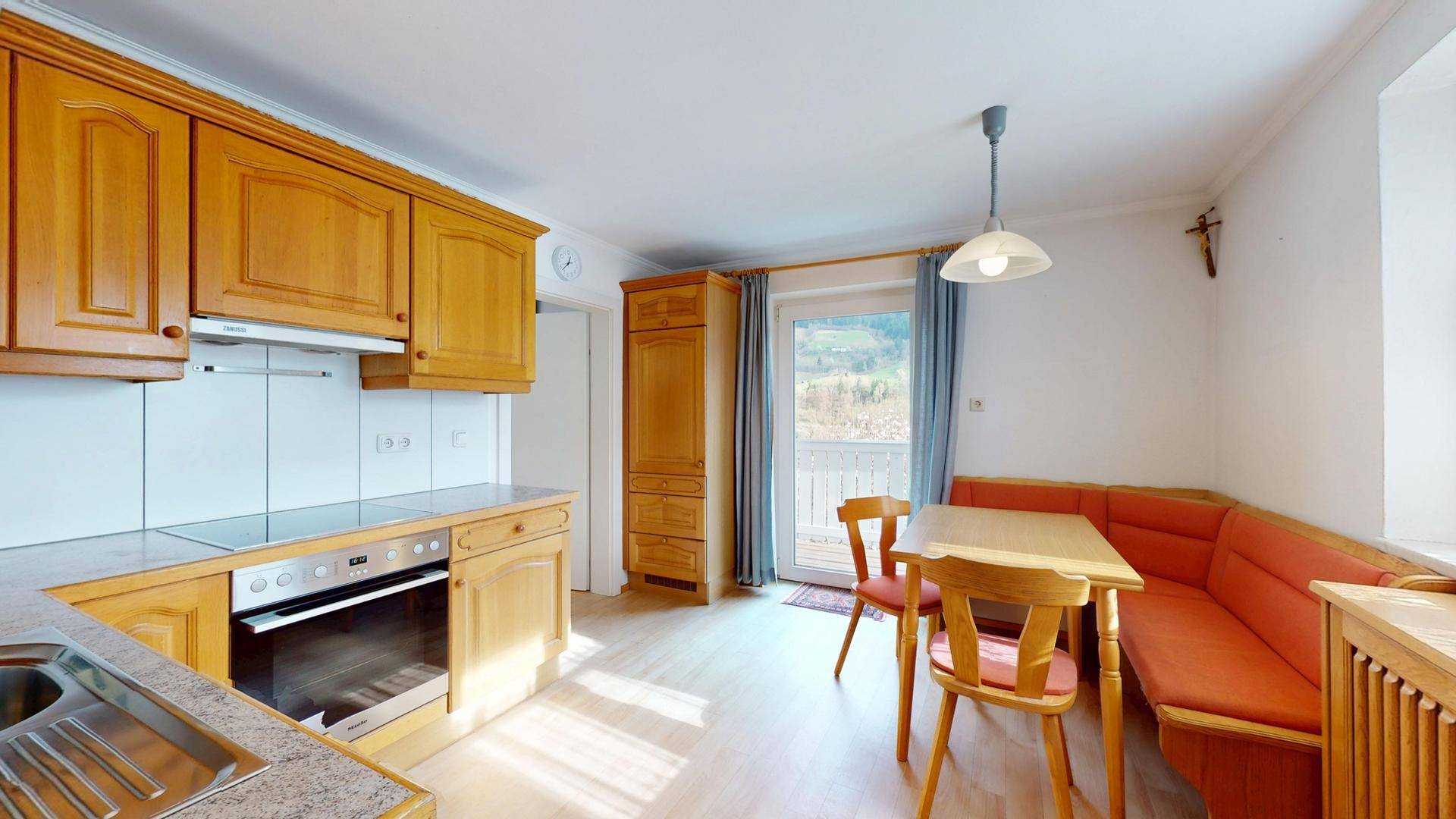 Traditionelle Wohnküche mit Holzeinbauten, Essecke und Zugang zum Balkon mit Bergblick.