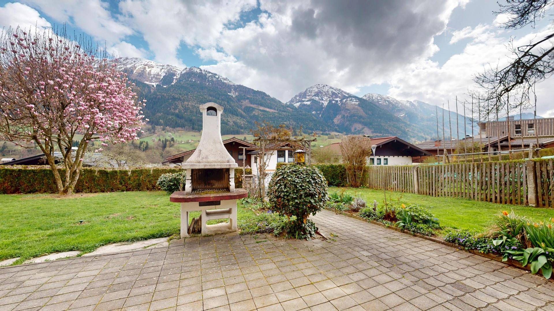 Gepflasterte Terrasse mit Grillplatz und weitläufigem Garten mit Bergblick.