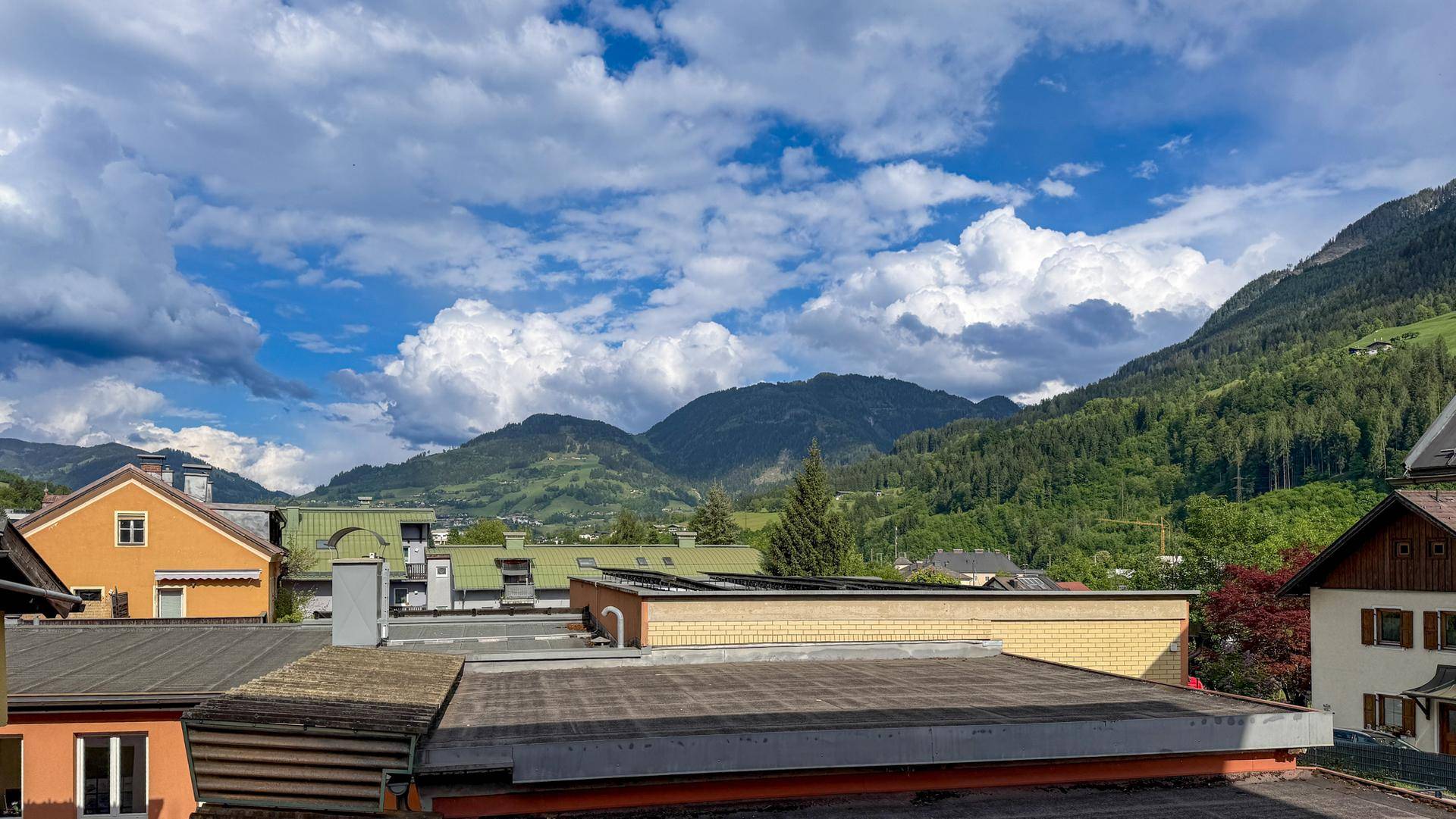 Panoramablick auf grüne Berge und Dächer von Gebäuden unter einem bewölkten Himmel, mit Solaranlagen.