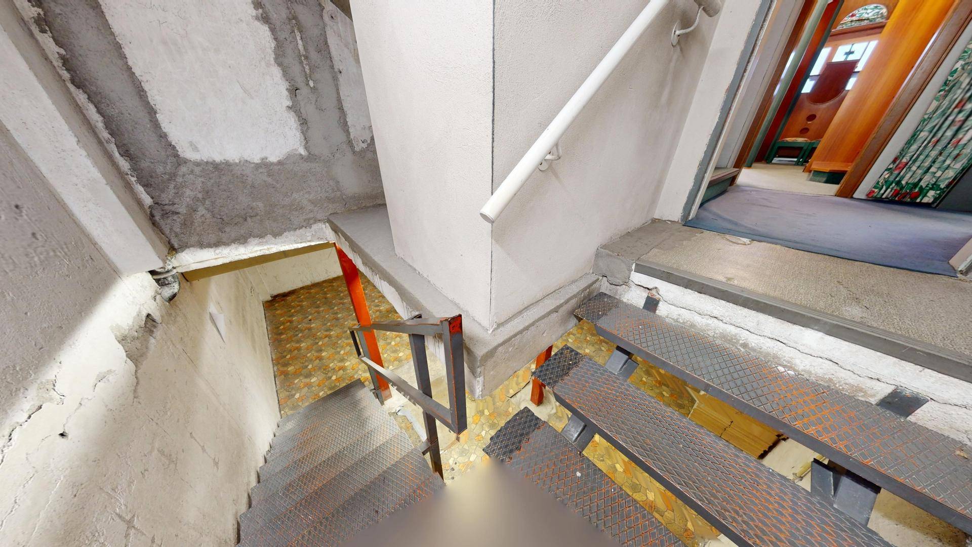 Treppenabgang in den Keller mit Metallstufen und rauen Betonwänden.