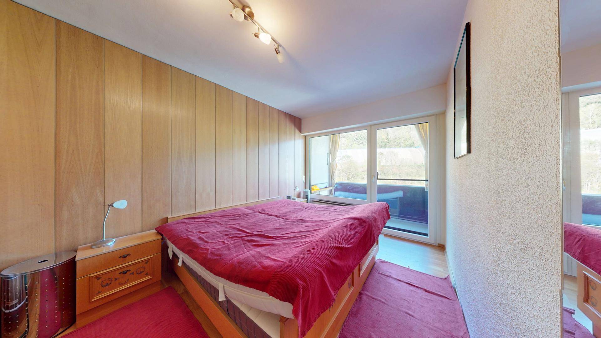 Schlafzimmer mit Doppelbett, Holzvertäfelung und Zugang zu einem Balkon.