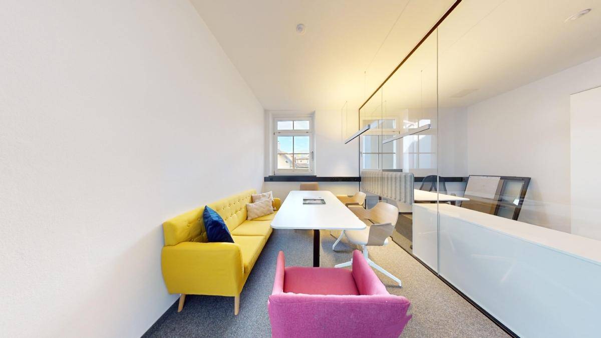 Heller Besprechungsraum mit einem gelben Sofa, einem modernen Tisch und einer Glaswand, die den Raum abtrennt.
