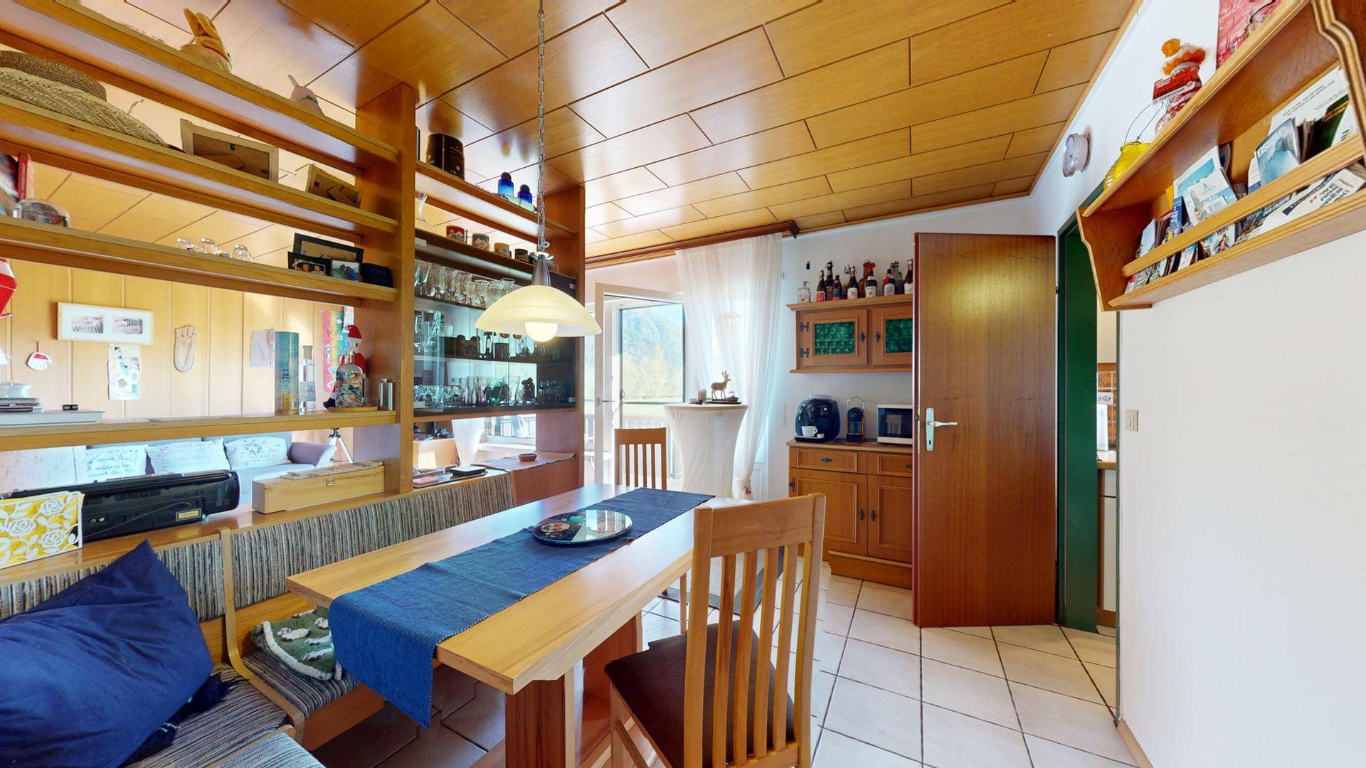 Traditioneller Essbereich mit Holztisch, Sitzbank und Vitrine, verbunden mit dem Wohnzimmer.