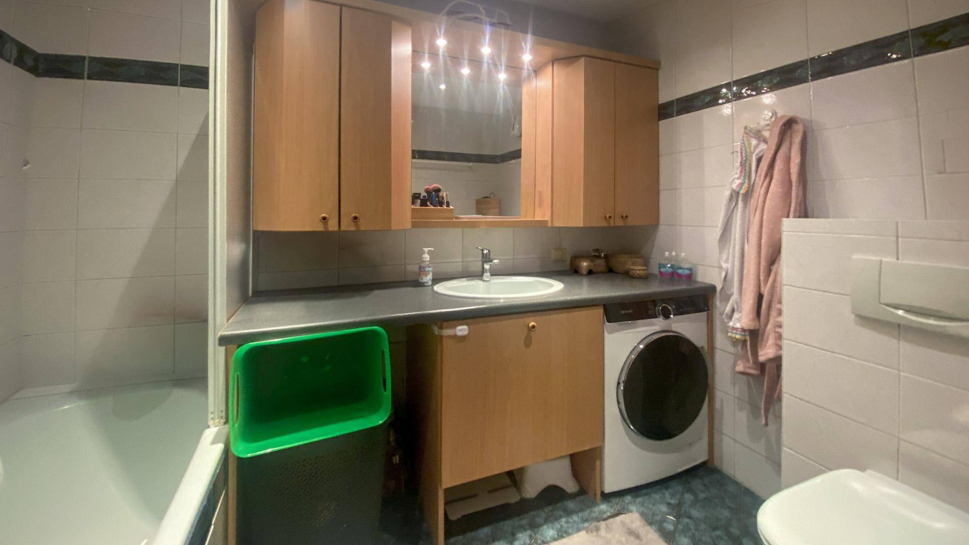 Badezimmer mit Badewanne, Waschmaschine, Waschbecken und Spiegelschrank.