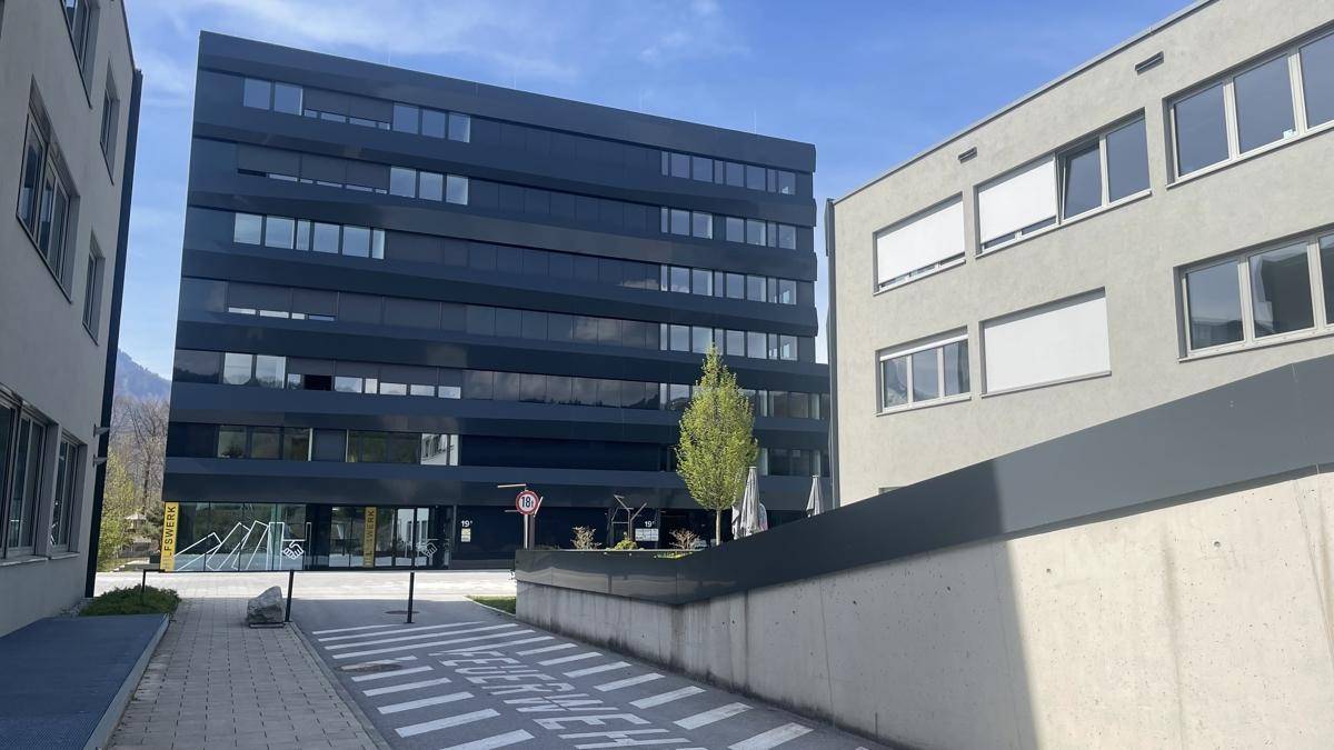 Moderne Bürogebäude mit dunkler Fassade und großen Fenstern unter bewölktem Himmel.